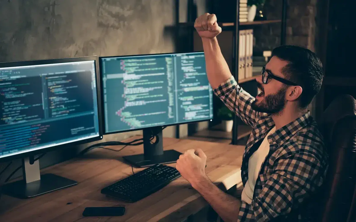 Un homme portant des lunettes célèbre à son bureau avec deux écrans affichant du code lié aux erreurs du site WordPress, les poings levés en signe de triomphe, dans une pièce faiblement éclairée.