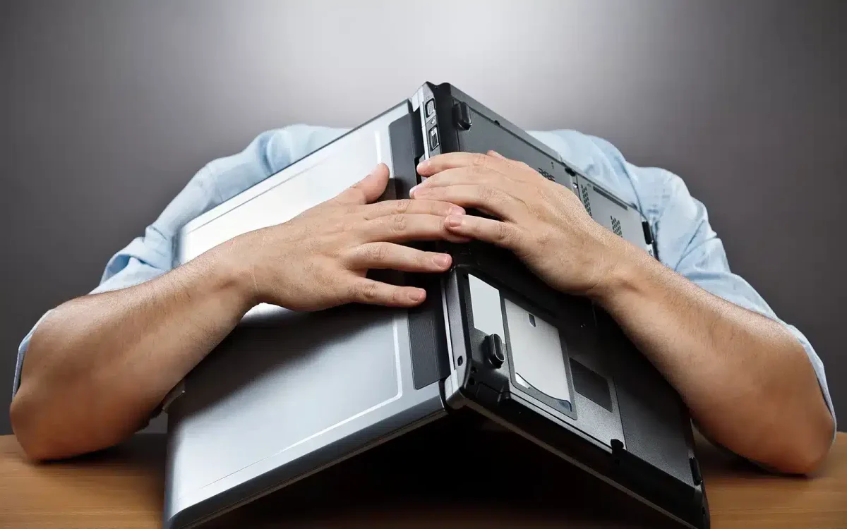 Une personne avec la tête baissée sur une table, partiellement masquée par un ordinateur portable affichant un site WooCommerce, les mains couvrant le haut de l'appareil.