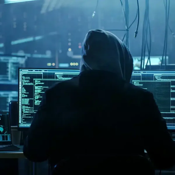 Une personne portant un sweat à capuche est assise à un bureau avec plusieurs écrans d'ordinateur affichant le code et les graphiques du site WooCommerce dans une pièce faiblement éclairée.