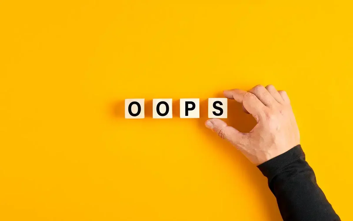 Une main disposant des blocs de bois qui épellent « OOPS » sur un fond jaune vif, rappelant les erreurs HTTP courantes sur un site WordPress.