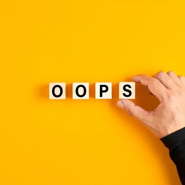 Une main disposant des blocs de bois qui épellent « OOPS » sur un fond jaune vif, rappelant les erreurs HTTP courantes sur un site WordPress.