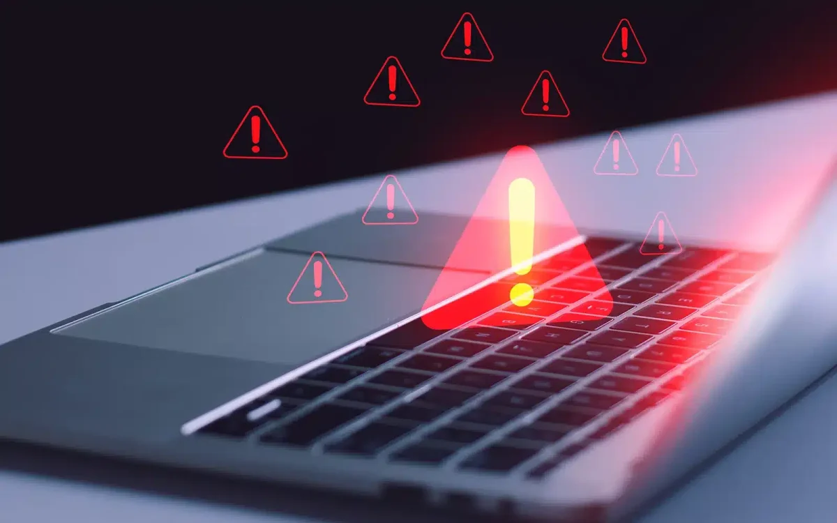 Clavier d'ordinateur portable avec plusieurs symboles d'avertissement rouges indiquant des alertes ou des problèmes, suggérant des malwares potentiels.