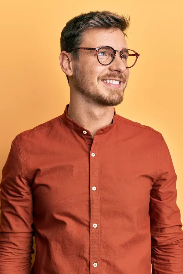 À propos de son personnage dynamique, on voit un homme aux cheveux bruns courts et à la barbe portant des lunettes et une chemise orange, souriant sur un fond jaune uni.