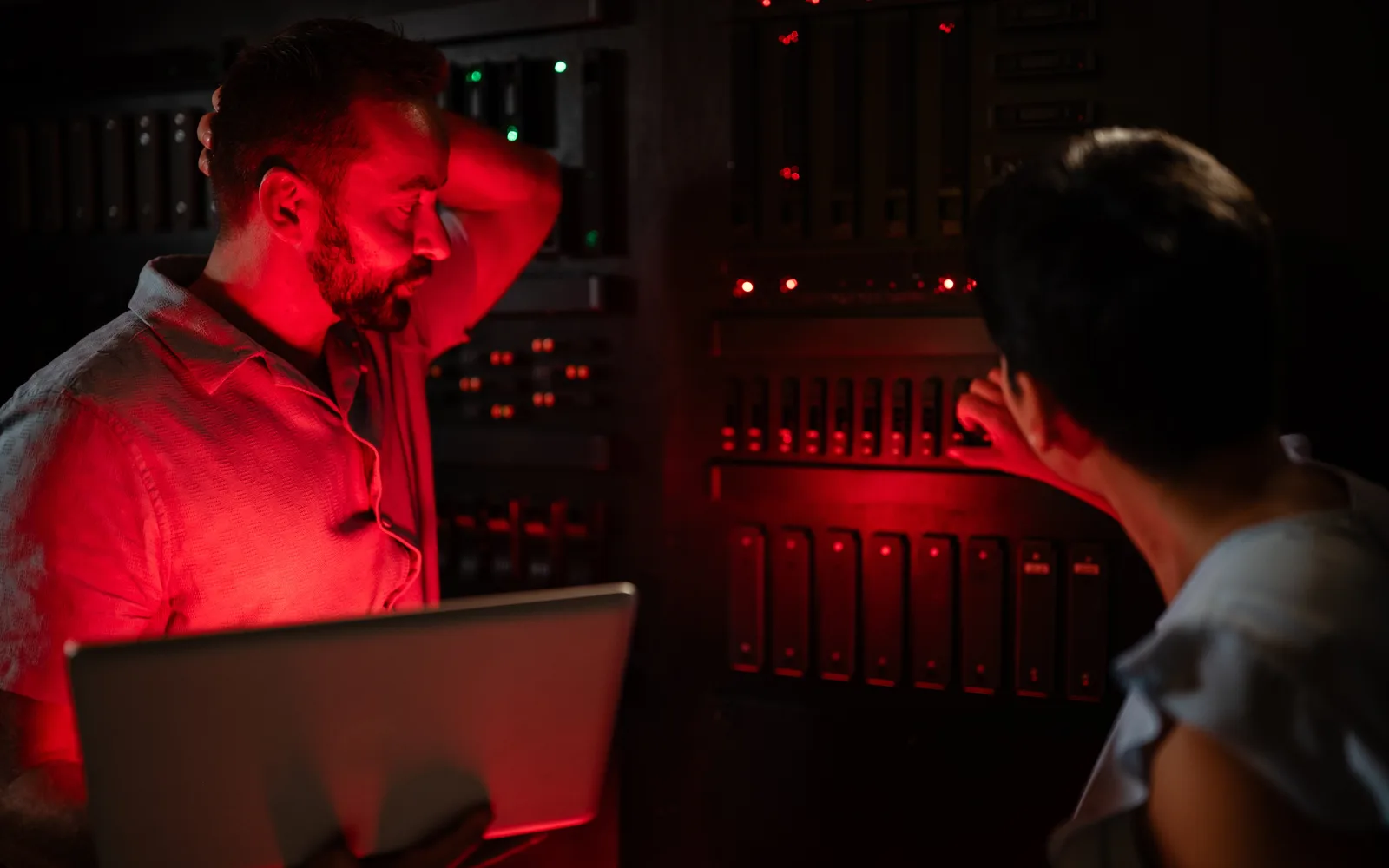 Deux techniciens dans une salle de serveurs plongée dans une lumière rouge d'alerte, l'un inquiet avec un ordinateur portable, l'autre qui intervient sur une baie, pour illustrer l'urgence de la faille PHP php2shell