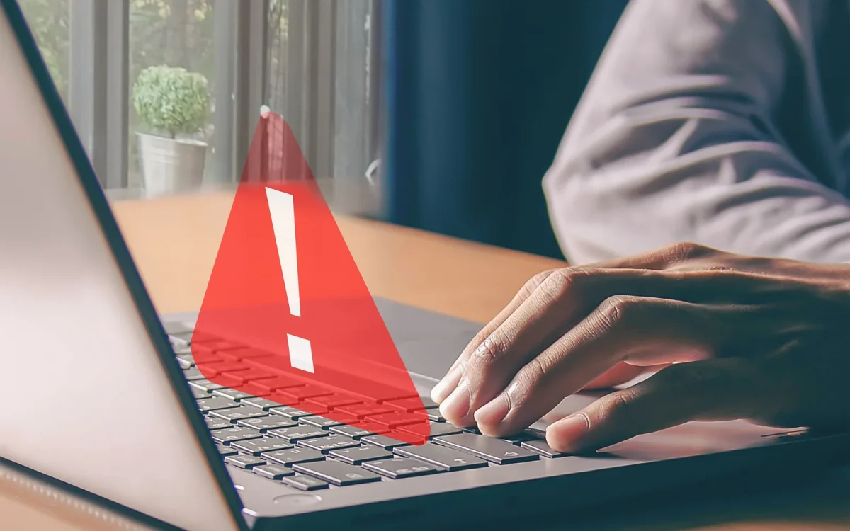 Mains sur le clavier d’un ordinateur portable affichant un triangle d’alerte rouge, symbole d’une faille de sécurité critique sur un site WordPress.