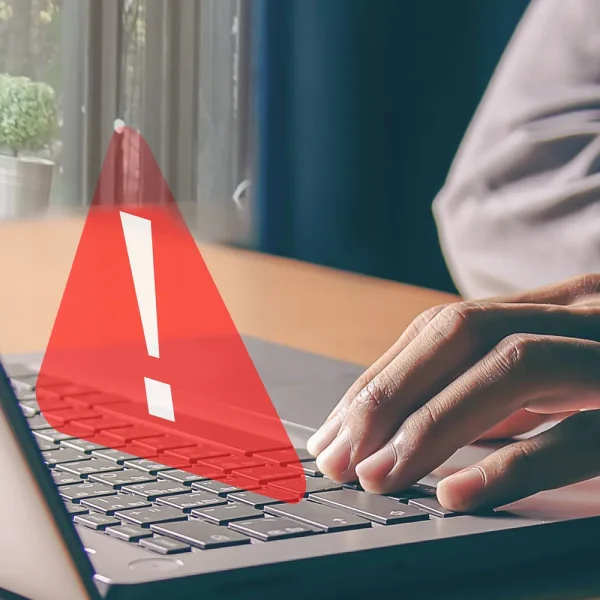 Mains sur le clavier d’un ordinateur portable affichant un triangle d’alerte rouge, symbole d’une faille de sécurité critique sur un site WordPress.