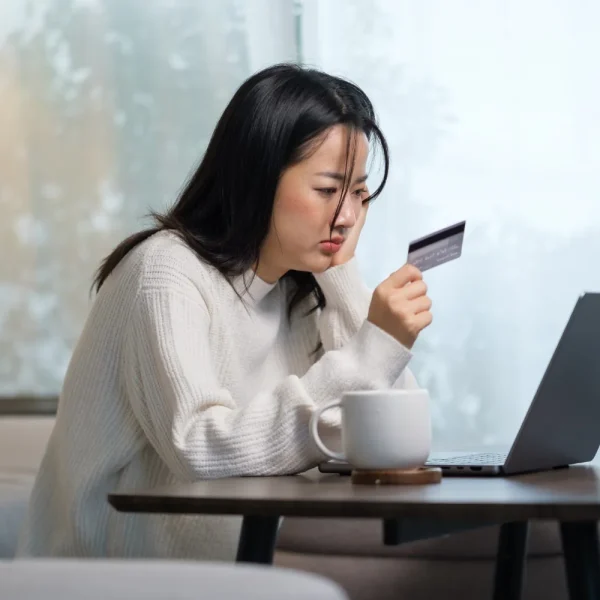 Cliente inquiète, carte bancaire en main devant son ordinateur portable, après un paiement refusé en ligne