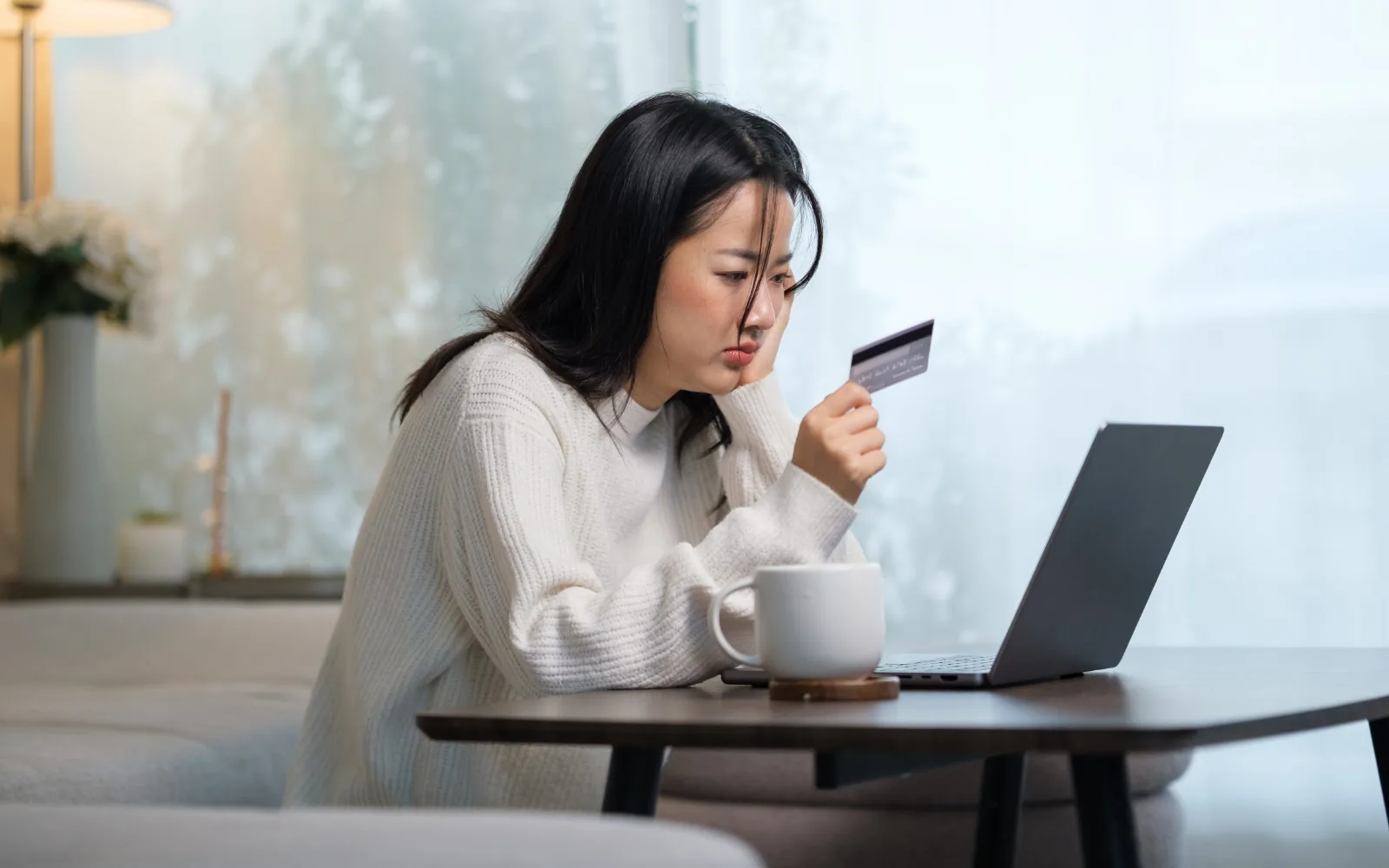 Cliente inquiète, carte bancaire en main devant son ordinateur portable, après un paiement refusé en ligne