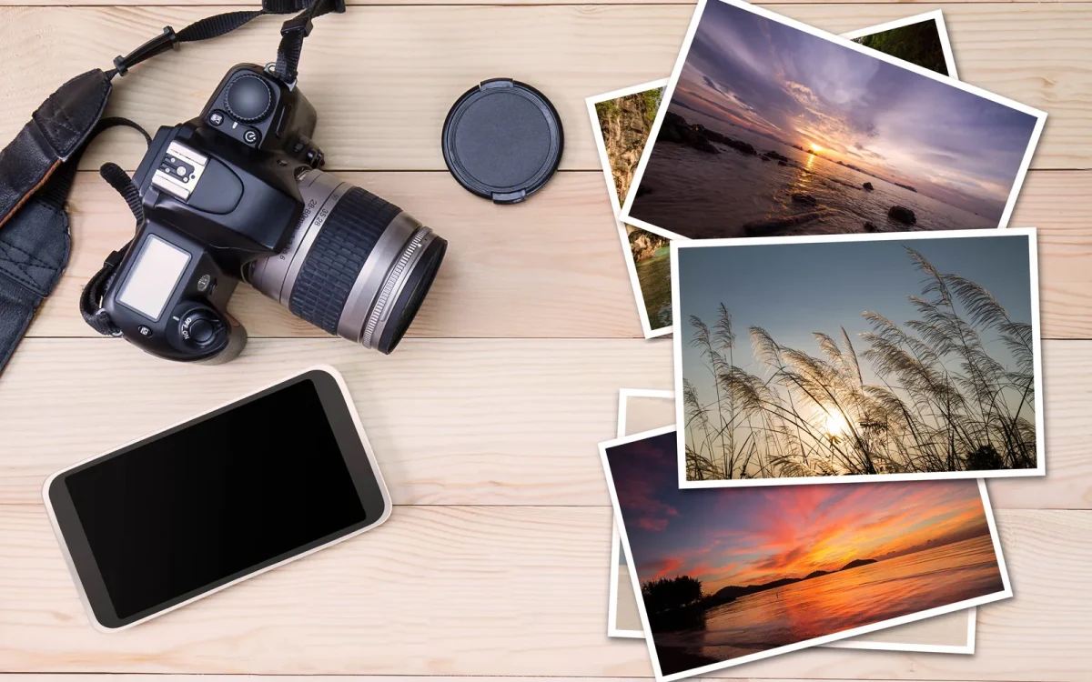 Appareil photo reflex, smartphone et tirages de photos de paysages posés sur une table en bois clair, pour illustrer le téléversement d'images dans la médiathèque WordPress