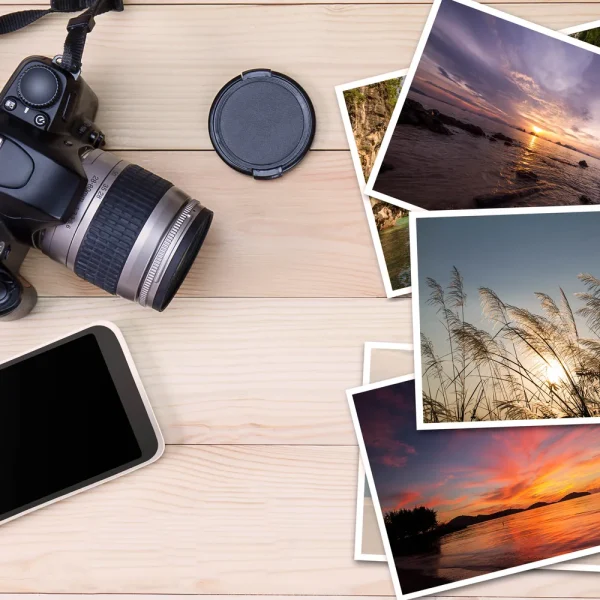 Appareil photo reflex, smartphone et tirages de photos de paysages posés sur une table en bois clair, pour illustrer le téléversement d'images dans la médiathèque WordPress