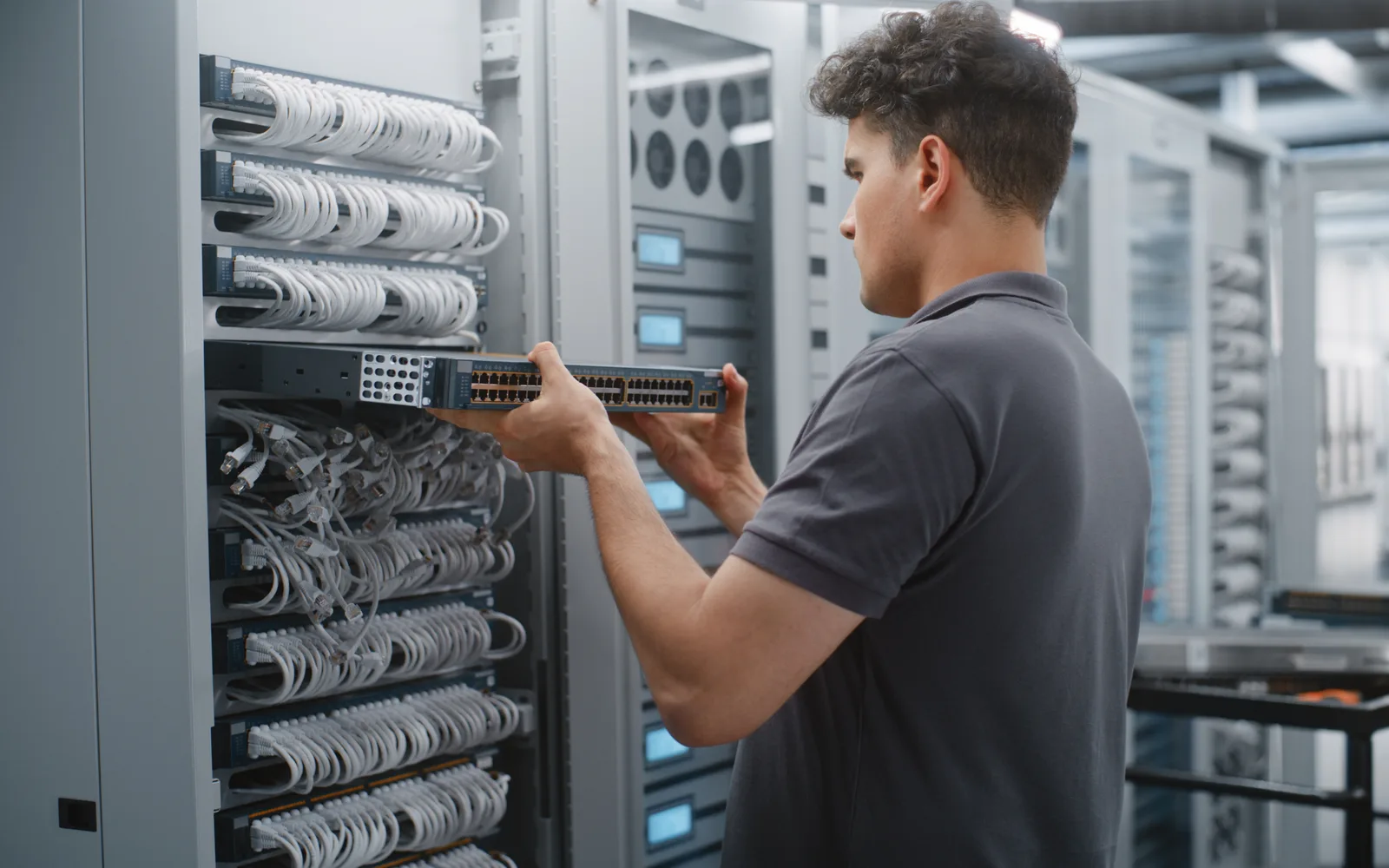 Technicien qui remplace un commutateur réseau dans une baie de serveurs lumineuse, pour illustrer la mise à jour de sécurité WordPress 7.1.4