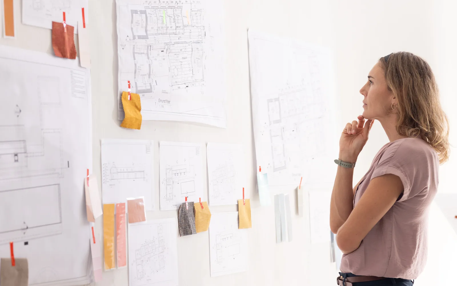 Femme pensive devant un mur couvert de plans et d’échantillons épinglés, qui prépare un projet, pour illustrer la préparation d’un site à WordPress 7.2